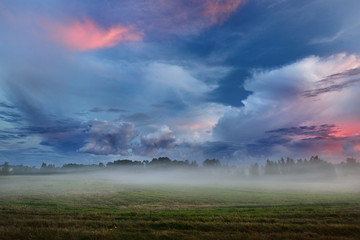 Obraz na płótnie Canvas Sunset over a misty field in countryside Latvia
