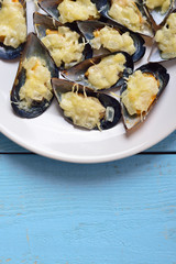 Plate with baked mussels with cheese and onions on a blue wooden