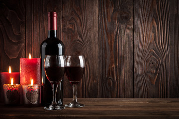 Red wine bottle, two glasses of wine and candles on the dark woo