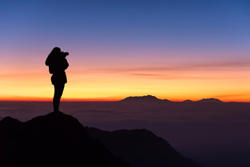 silhouette of woman taking photograph on the top of mountain and