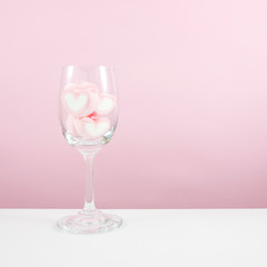 The lovely pink heart marshmallows in wine glass on white table.