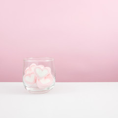 The lovely pink heart marshmallows in small round glass on white table.