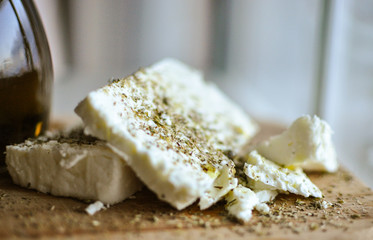 close up of feta cheese(Greek cheese) slices on a wooden serving board  and a bottle of olive oil...