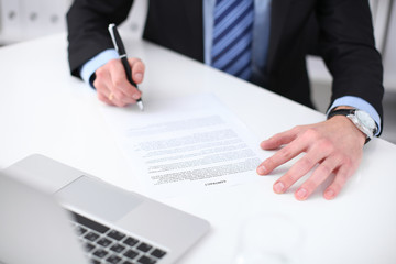 Young business man signs contract sitting at the desk in office