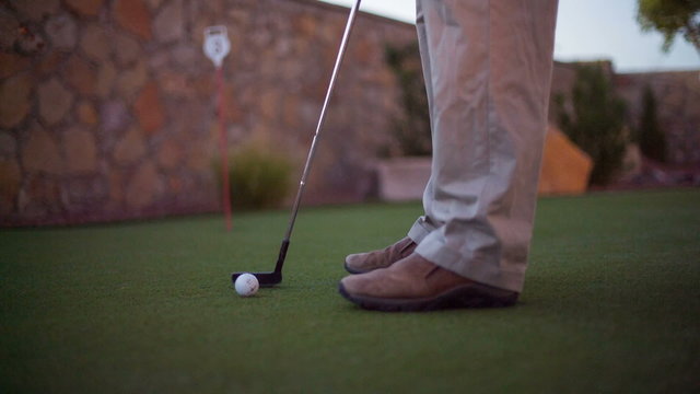 Making Golf Putt on Practice Green. camera moves down as a player putts in a golf ball on a practice green in the backyard
