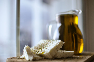 feta cheese(Greek cheese) slices on a wooden serving board  and a bottle of olive oil in nature light © Mahi