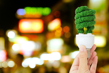 hand holding green light bulb and defocused city night light background, eco energy concept