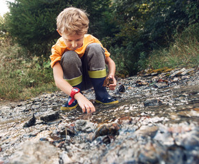 Boy in gum boots playing the into te forest stream