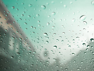 Raindrops on car's glass with blurry cloudy sky in village. Gree