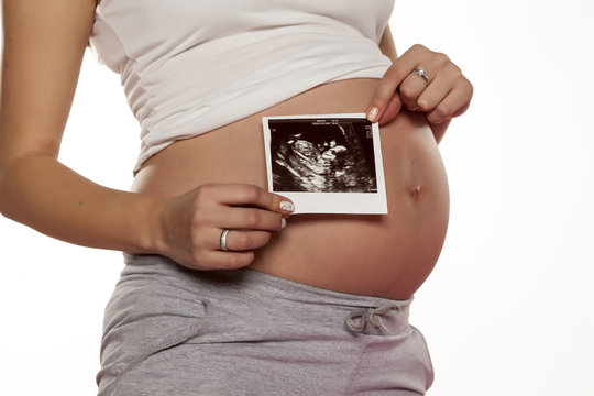 pregnant woman holding  the picture of the ultrasound on her belly