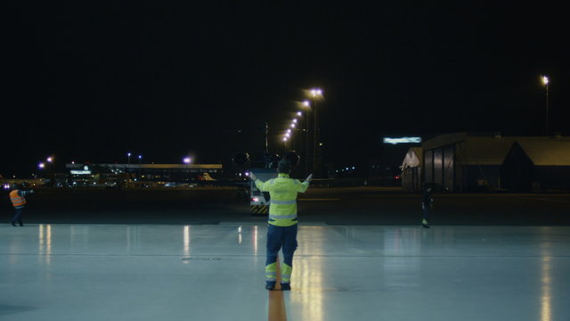 Aircraft coordinator signals an airplane in the night to move towards hangar. Shot on RED Cinema Camera.