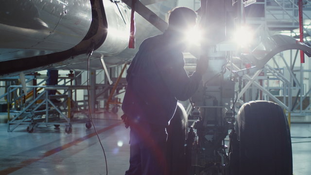 Aircraft maintenance mechanic with a flash light inspects plane chassis in a hangar. Shot on RED Cinema Camera.