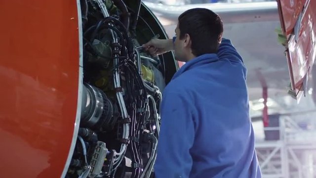 Aircraft maintenance mechanic inspects and tunes plane engine in a hangar. Shot on RED Cinema Camera.