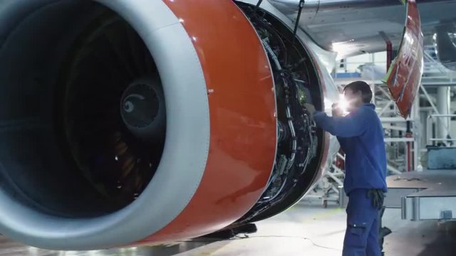 Aircraft maintenance mechanic with a flash light inspects plane engine in a hangar. Shot on RED Cinema Camera.