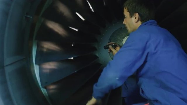 Aircraft maintenance mechanic with a flash light inspects plane turbine blades in a hangar. Shot on RED Cinema Camera.
