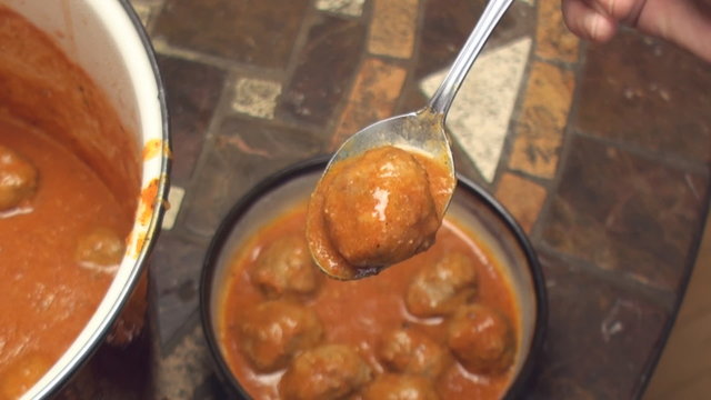 Serving homemade meatballs in porcelain bowl. Close up of meatball with tomato sauce on the spoon.