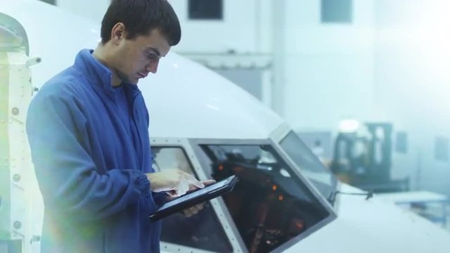 Aircraft maintenance mechanic uses tablet in front of a airplane cabin in a hangar. Shot on RED Cinema Camera.