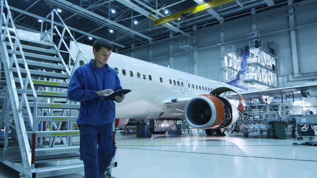 Aircraft maintenance mechanic in blue uniform is going down the stairs while using tablet in a hangar. Shot on RED Cinema Camera.