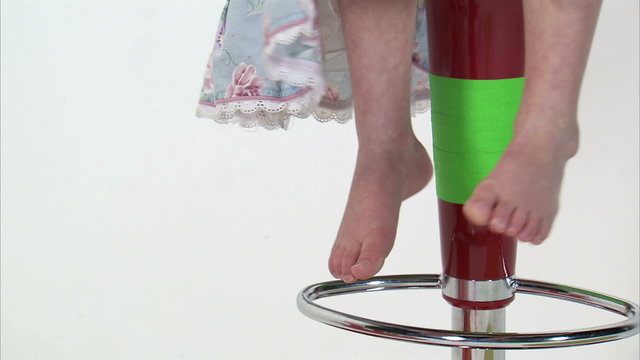 Royalty Free Stock Footage of Young girl's feet swinging while sitting on a tall chair.