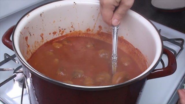 Mixing home made meatballs with tomato sauce in the red big pot.