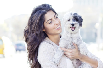 Young beautiful woman smiling and  hugging her small poodle dog on the street