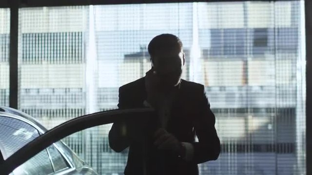 Businessman gets out of a black executive car in the afternoon while speaking on a phone. Shot on RED Cinema Camera.