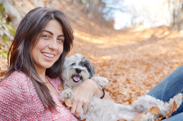 smiling woman laying in the autumn forest with her small poodle dog