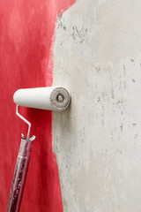 White paint roller and red paint on white wall