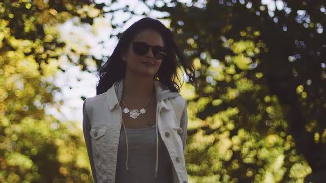 Beautiful girl with sunglasses in an orchard, walking toward the camera, in slow motion with bokeh