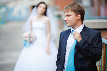 The groom dark blue suit straightens turquoise tie with a sour face, in background tired and...