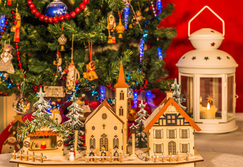 Деревянные игрушечные домики на фоне новогодней елки с фонарем со свечой.