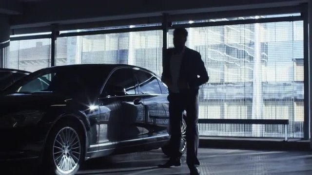 Businessman in a suit gets out of a black executive car in a garage parking lot. Shot on RED Cinema Camera.