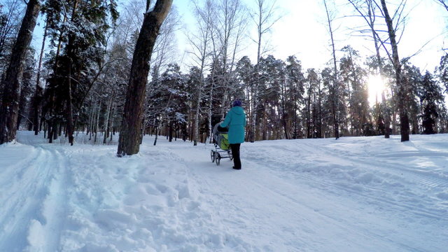 The girl with the baby in a carriage on walk in winter wood. 