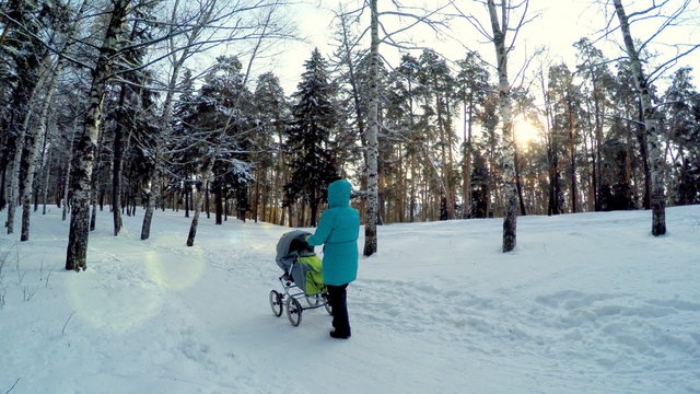 The girl with the baby in a carriage on walk in winter wood. 