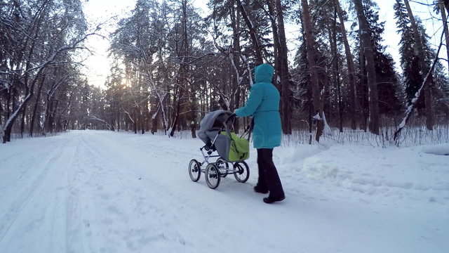 The girl with the baby in a carriage on walk in winter wood. 
