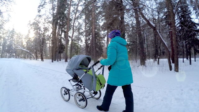 The girl with the baby in a carriage on walk in winter wood. 