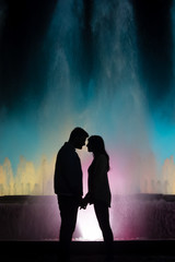 silhouette of two lovers with colorful fountain background.