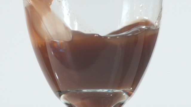 Close up of elongated tulip shaped wine glass filled with a brown liquid in slow motion