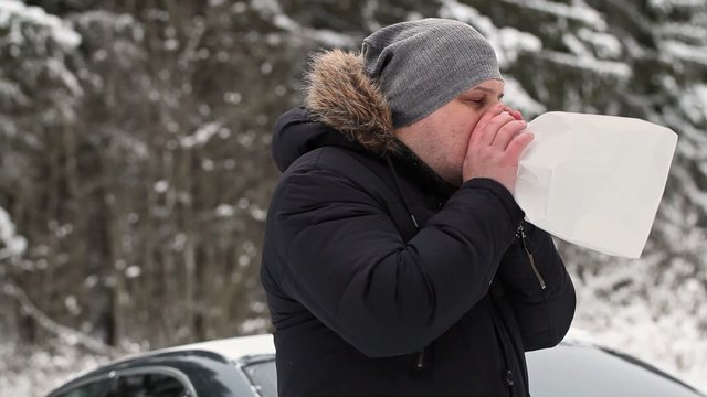 Stressful man after accident breathe into paper bag near car on snowy road