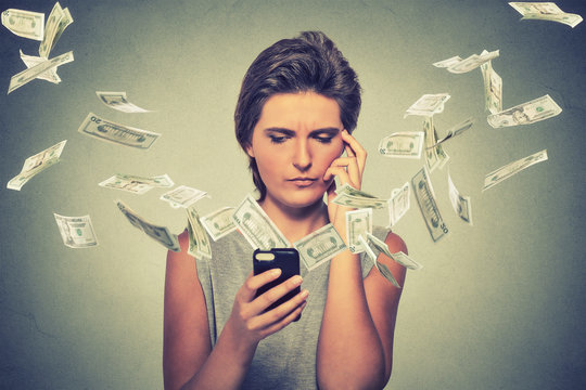 Thoughtful young woman using smartphone with dollar bills banknotes flying away