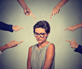 Sad embarrassed woman in glasses looking down many fingers pointing at her