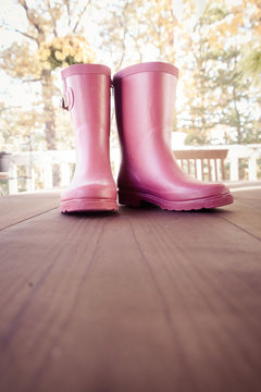 Pink rain boots on wooden surface during autumn; vertical image