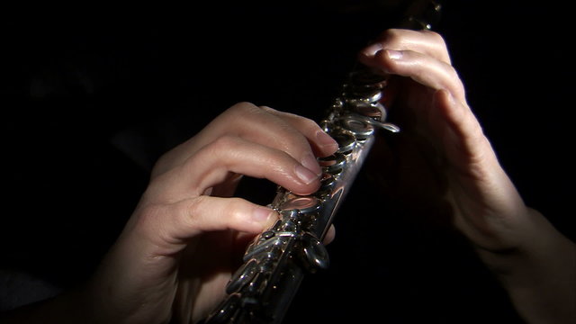 Hands playing a flute on a black background.
