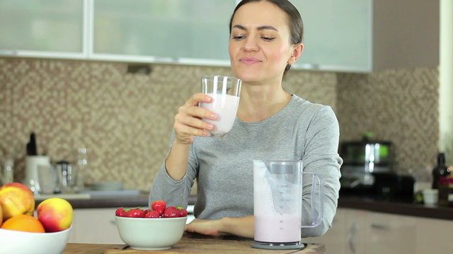 Young brunette woman drinking strawberries milk shake and smiling in front of camera