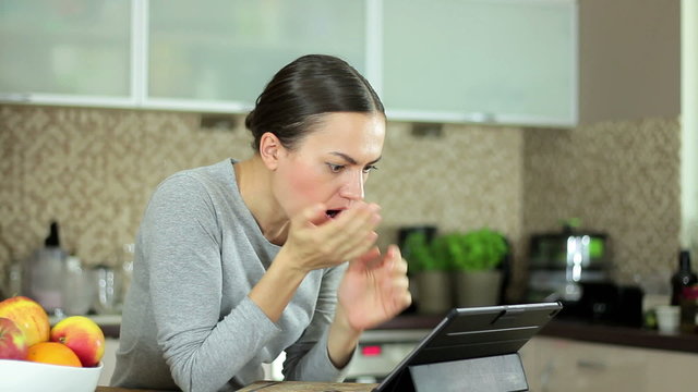 Surprised young woman looking at the tablet computer while sitting in the kitchen