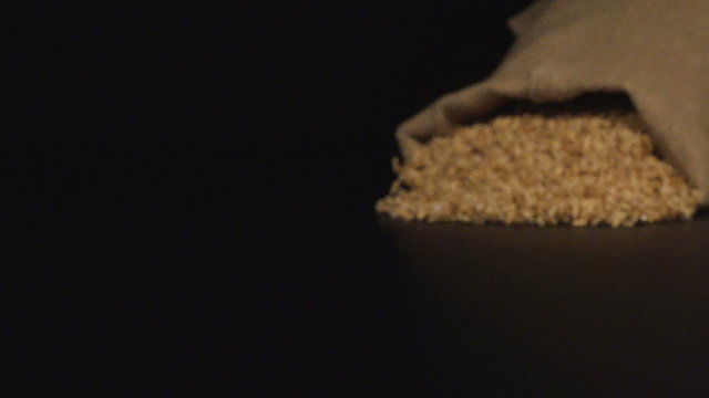 SLOW (240fps): A cloth bag falls on a table and a oats scatter out it

