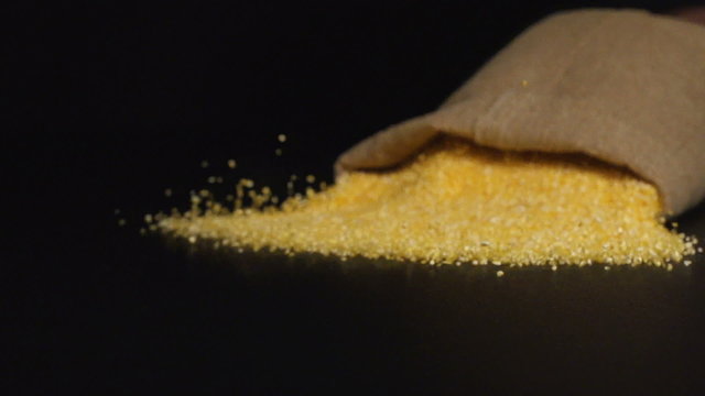 SLOW (240fps): A cloth bag falls on a table and a corn grits scatter out it
