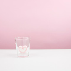 The lovely pink heart marshmallow in shot glass on white table.