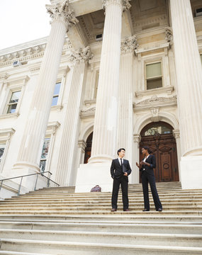 A well dressed man and woman converse on the steps of a legal or municipal building. Could be business or legal professionals or lawyer and client.