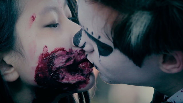 Male and female teenagers with scary makeup on faces kissing at Halloween party
